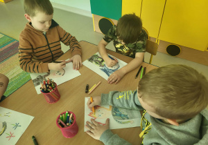 Kilkoro dzieci przy stole przy rysuje autoportret.