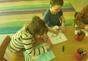 Kilkoro dzieci przy stole przy rysuje autoportret.