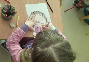 Kilkoro dzieci przy stole przy rysuje autoportret.