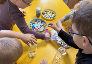 Dzieci wkładają do butelek wybrane ozdoby.