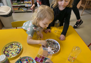 Dzieci wkładają do butelek wybrane ozdoby.