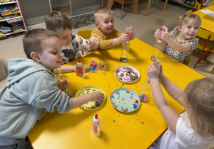 Dzieci wkładają do butelek wybrane ozdoby.