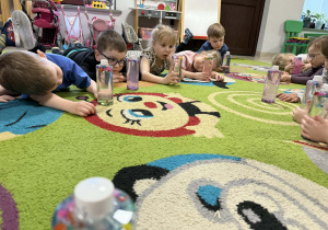 Dzieci oglądają przygotowane przez siebie butelki.