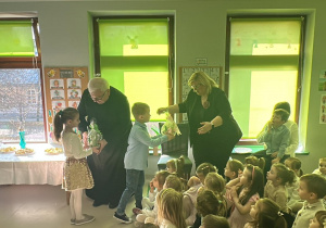 Wybrane dzieci starsze wręczają upominki Gościom.