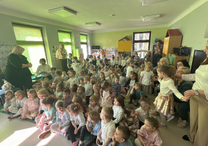 Odświętnie ubrane przedszkolaki wraz z paniami w trakcie wielkanocnego spotkania z Księdzem.
