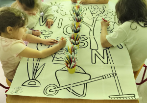 Młodsze dziewczynki wraz ze starszymi koleżankami kolorują elementy wybranymi przez siebie mazakami.