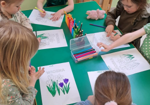 Kilkoro dzieci z grupy "Żabek" przy stole koloruje szablon wiosennych kwiatów.