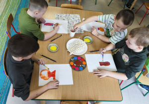 Kilkoro dzieci z grupy "Pszczółek" przy stole maluje wazon, a w nim gałązki forsycji.