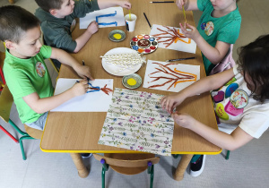 Kilkoro dzieci z grupy "Pszczółek" przy stole maluje wazon, a w nim gałązki forsycji.