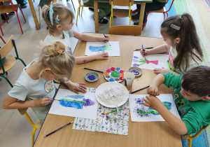 Kilkoro dzieci z grupy "Pszczółek" przy stole maluje wazon, a w nim kwitnące hiacynty.