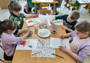 Kilkoro dzieci z grupy "Pszczółek" przy stole maluje wazon, a w nim kwitnące hiacynty.
