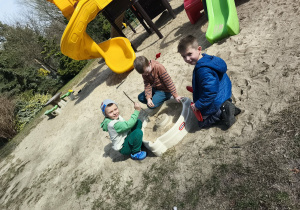 Chłopcy konstruują budowle z piasku na przedszkolnym placu zabaw.