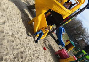 Dzieci zjeżdżają ze zjeżdżalni na ogrodzie przedszkolnym.