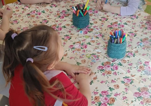 Kilkoro dzieci z najmłodszej grupy przy stoliku koloruje mazakami drewniane pisanki.