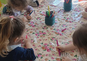 Kilkoro dzieci z najmłodszej grupy przy stoliku koloruje mazakami drewniane pisanki.