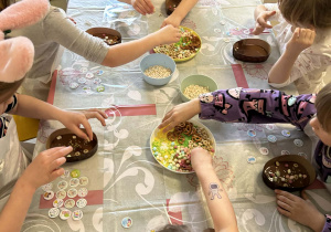 Kilkoro dzieci z grupy "Motylków" dekoruje swoją, czekoladową pisankę przy użyciu kolorowych, jadalnych ozdób.