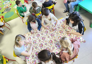 Kilkoro dzieci z grupy V przy stole zdobi torebkę przy użyciu świątecznych naklejek.