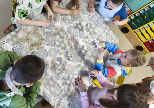 Kilkoro dzieci z grupy V przy stole zdobi torebkę przy użyciu świątecznych naklejek.