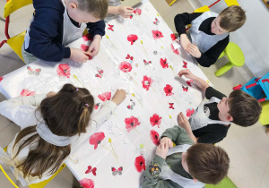 Kilkoro dzieci z grupy V przy stole zdobi torebkę przy użyciu świątecznych naklejek.