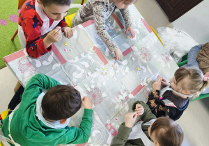 Kilkoro dzieci z grupy V przy stole zdobi torebkę przy użyciu świątecznych naklejek.