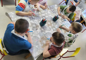 Kilkoro dzieci z grupy V koloruje drewnianą pisankę przy użyciu mazaków.