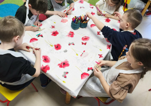 Kilkoro dzieci z grupy V koloruje drewnianą pisankę przy użyciu mazaków.