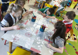 Kilkoro dzieci z grupy V koloruje drewnianą pisankę przy użyciu mazaków.