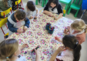 Kilkoro dzieci z grupy V koloruje drewnianą pisankę przy użyciu mazaków.