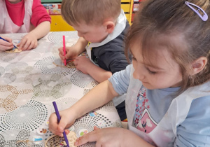 "Żabki" ozdabiają drewnianą pisankę przy użyciu kolorowych mazaków.