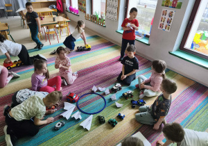 Dzieci parkują swoje, zabawkowe/papierowe pojazdy wokół obręczy.