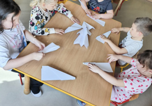 Chętne dzieci, przy wsparciu nauczycielki tworzą swoje, papierowe samoloty.