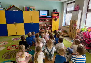 Dzieci z grupy "Wiewiórek" siedzą na dywanie i oglądają prezentację nt. autyzmu.