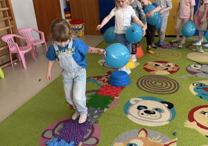 "Wiewiórki" przechodzą boso po ścieżce sensorycznej z balonikami w dłoniach.
