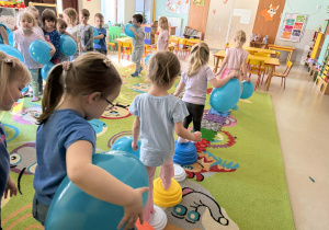 "Wiewiórki" przechodzą boso po ścieżce sensorycznej z balonikami w dłoniach.