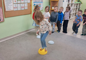 Dzieci z grupy "Żabek" kolejno przechodzą boso po ułożonych elementach na dywanie.
