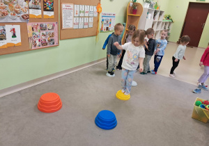Dzieci z grupy "Żabek" kolejno przechodzą boso po ułożonych elementach na dywanie.