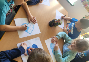 Kilkoro dzieci z grupy "Pszczółek" koloruje szablon serca na kolor niebieski, po czym go wycina.