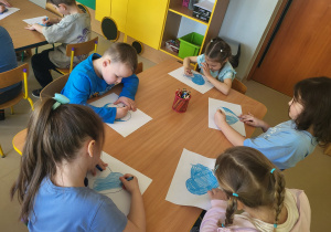 Kilkoro dzieci z grupy "Pszczółek" koloruje szablon serca na kolor niebieski, po czym go wycina.