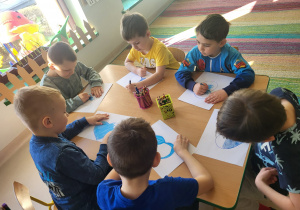 Kilkoro dzieci z grupy "Pszczółek" koloruje szablon serca na kolor niebieski, po czym go wycina.