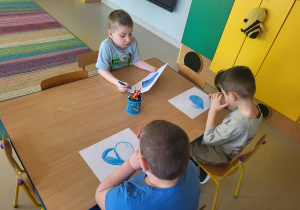 Kilkoro dzieci z grupy "Pszczółek" koloruje szablon serca na kolor niebieski, po czym go wycina.