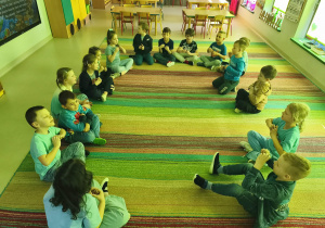 "Pszczółki" siedząc w kręgu śpiewają refren piosenki wraz z nauczycielką.