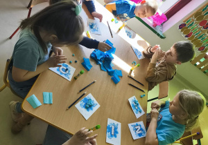 "Pszczółki" formują kuleczki z niebieskiej bibuły i wyklejają nimi wybrane przez siebie litery.