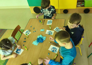 "Pszczółki" formują kuleczki z niebieskiej bibuły i wyklejają nimi wybrane przez siebie litery.