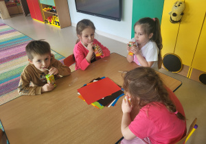 Dzieci siedząc przy stole, wypijają soczki z kartoników.