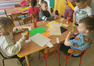 Kilkoro dzieci przy stole tworzy swój autokar dla przyjaciół, korzystając z kartonów po soczkach i kolorowego papieru.