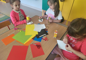 Kilkoro dzieci przy stole tworzy swój autokar dla przyjaciół, korzystając z kartonów po soczkach i kolorowego papieru.