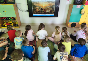 Dzieci siedząc na dywanie, dowiedziały się, dlaczego historia Stumilowego Lasu przetrwała 100 lat.