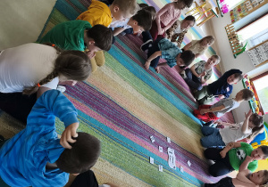 Dzieci siedzą na dywanie i podają zdrowe zamienniki dla bohaterów historyjki(Asi i Karola), którzy zbyt często sięgali po słodkie i słone przekąski.