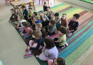 Dzieci siedzą na dywanie i oglądają prezentację na temat naszej planety - Ziemi.