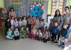 Grupowe zdjęcie dzieci wraz z paniami z grupy "Żabek" na tle przygotowanej wcześniej dekoracji tematycznej.